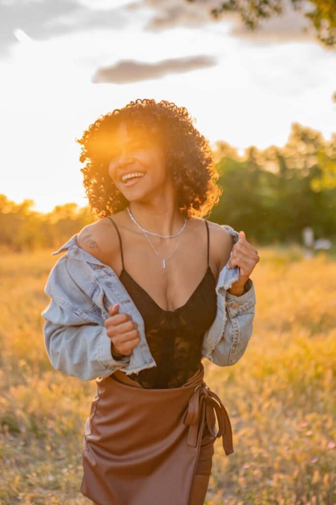 A smiling woman enjoys the warm glow of sunset in a field.