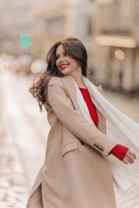 Chic woman smiling in a fashionable beige coat and scarf, exuding elegance and joy.